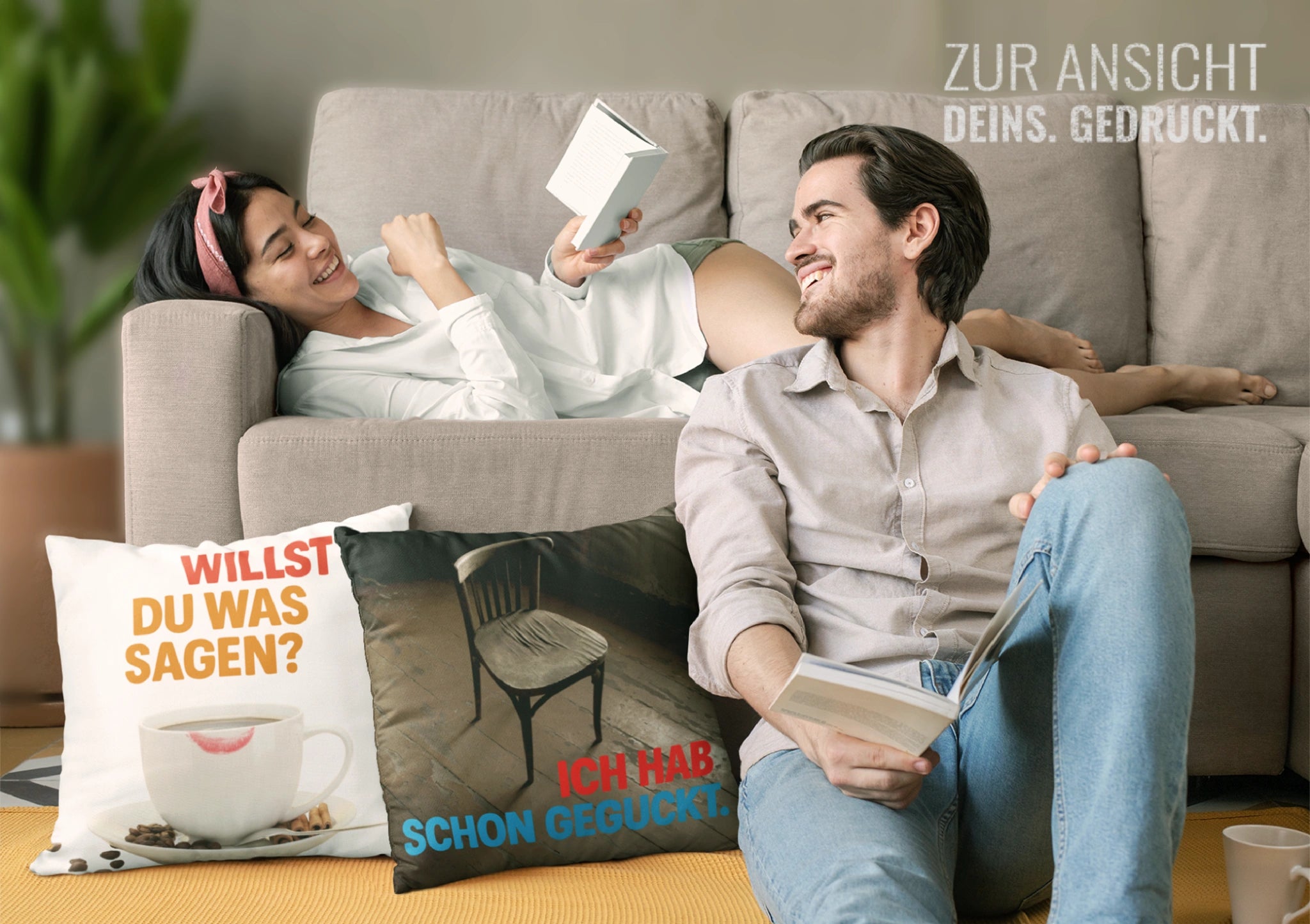 Zwei Menschen auf dem Sofa, davor zwei Kissen mit Sprüchen: „Willst du was sagen?“ und „Ich hab schon geguckt.“ – entspannte Leseatmosphäre.